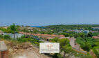 Panoramablick vom Baugrundstück in Cala Romántica: Villen, Pinienwald und Meerblick unter blauem Himmel.