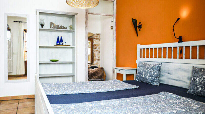 Schlafzimmer mit zwei Einzelbetten, orangefarbener Akzentwand, weißem Holzrahmen und Rattanlampe im Agroturismo Ses Salines