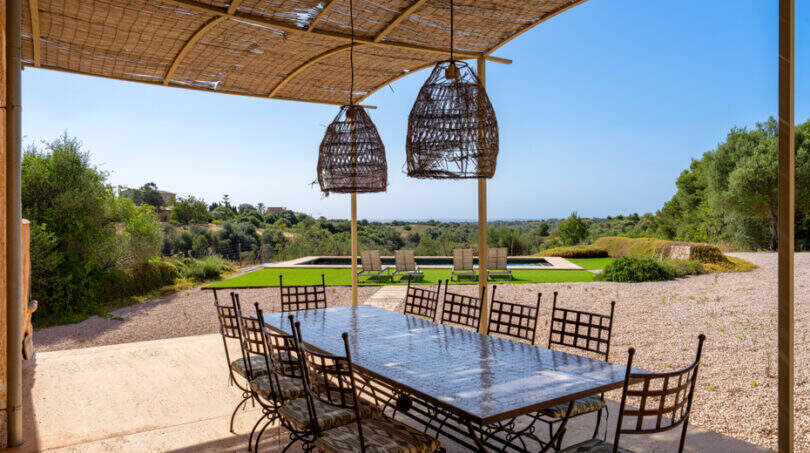 Überdachte Außenterrasse mit Esstisch, Korblampen und Blick auf Pool und Meer in Finca Cales de Mallorca