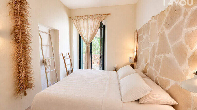 Helles Schlafzimmer mit Doppelbett, Natursteinwand und Terrassentür in historischer Wohnung in Ses Salines.