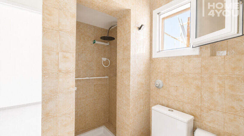 Badezimmer mit beigen Fliesen, Dusche, WC und Fenster in Erdgeschosswohnung nahe Strand Cala Llombards