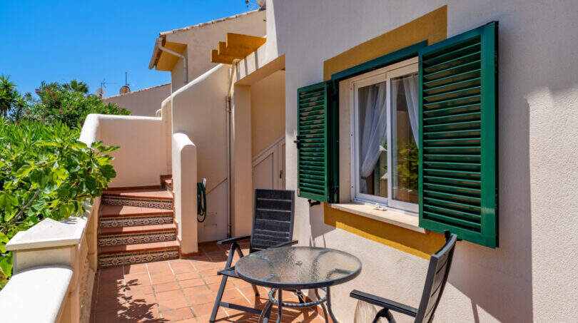 Sonnige Terrasse mit Bistrotisch, grünen Fensterläden und Fliesentreppe in Cala Murada
