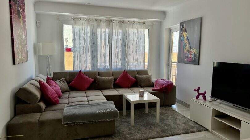 Helles Wohnzimmer mit großem Ecksofa, rosa Kissen, Flachbild-TV und Zugang zum Balkon in Strandnähe, Palma de Mallorca