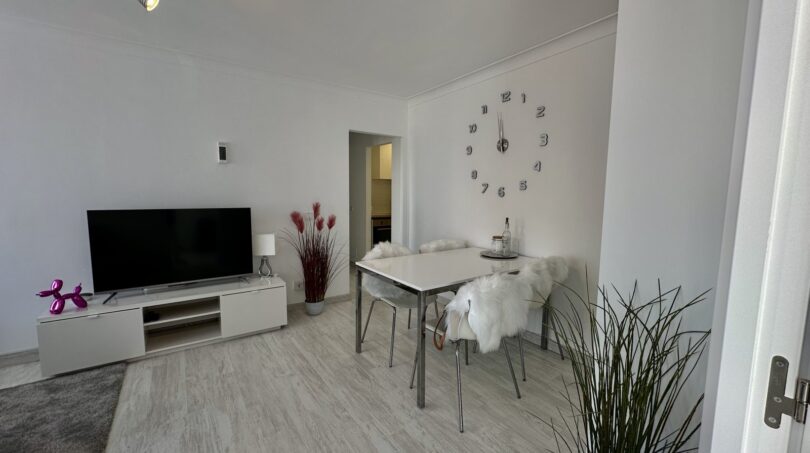 Helles Wohnzimmer mit TV-Möbel, Esstisch und Wanduhr in modernisierter Strandwohnung Palma de Mallorca