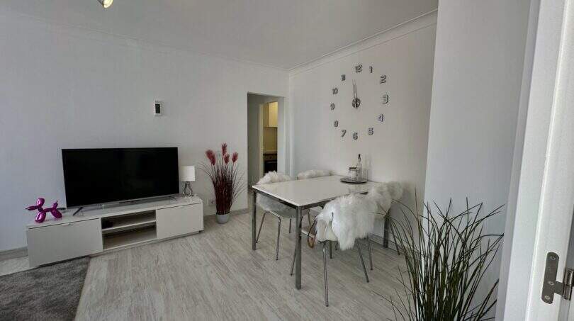 Helles Wohnzimmer mit TV, modernem Esstisch und dekorativer Wanduhr in strandnaher Wohnung in Palma