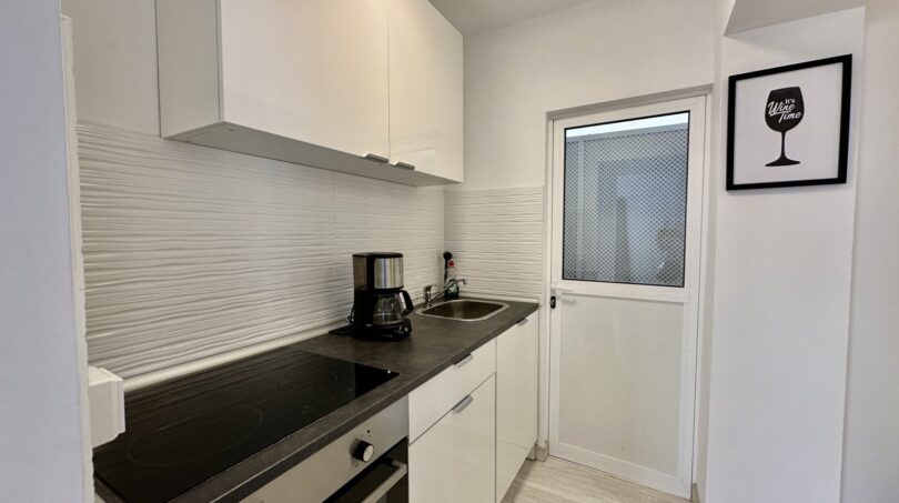 Moderne weiße Küche mit Cerankochfeld, Kaffeemaschine und Spüle in strandnaher Wohnung in Palma de Mallorca.