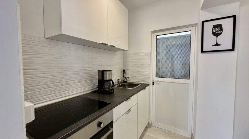 Moderne weiße Küche mit Induktionskochfeld, Kaffeemaschine, Spüle und Weinzeit-Wandbild in Strandwohnung Palma
