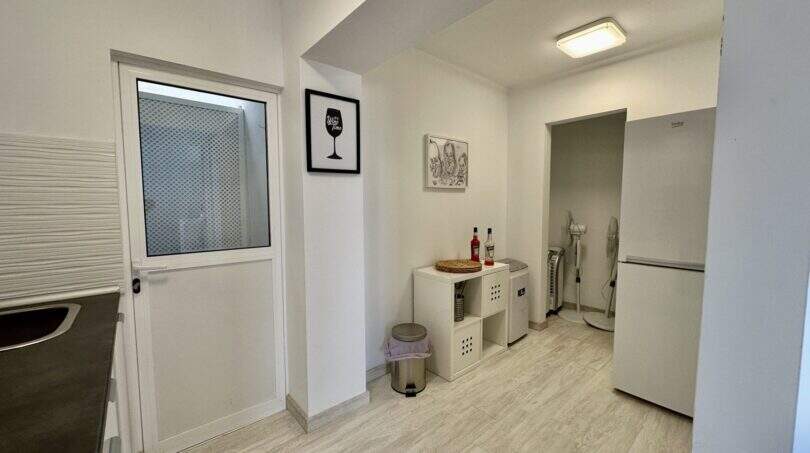 Helle Küche mit Laminatboden, weißen Regalen, Weinflaschen und modernen Wandbildern in Strandwohnung Palma