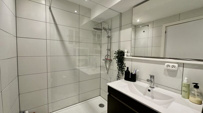 Modernes Badezimmer mit Regendusche, weißen Großformatfliesen, Waschtisch und Spiegel in Strandwohnung Palma