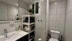 Modernes Badezimmer mit weißen Fliesen, Waschbecken, WC und Regaleinheit mit Handtüchern in der Strandwohnung Palma