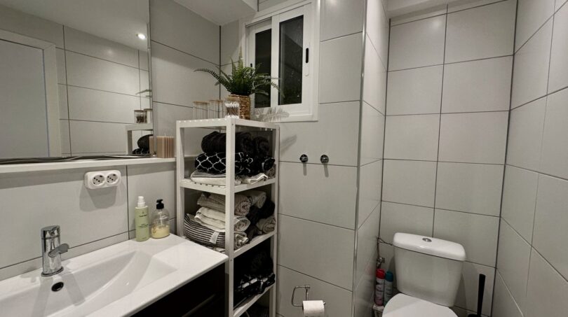 Modernes Badezimmer mit weißen Fliesen, Waschbecken, WC und Regal mit Handtüchern in Strandwohnung Palma