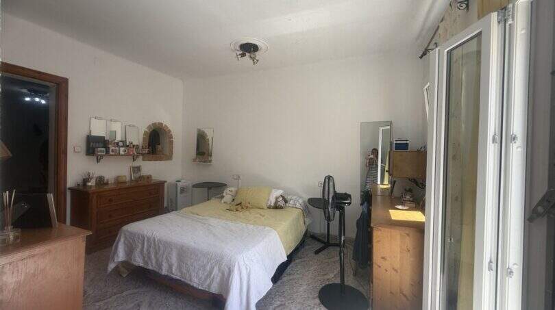 Helles Schlafzimmer der Wohnung in Inca mit Doppelbett, Holzmöbeln, Spiegel und Zugang zum Balkon.