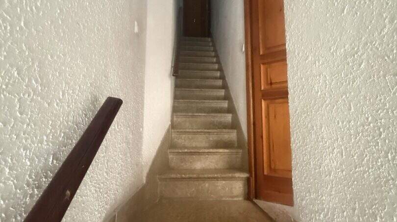 Schmales Treppenhaus mit Steinstufen, Holzhandlauf und Holztür in charmanter Wohnung in Inca.