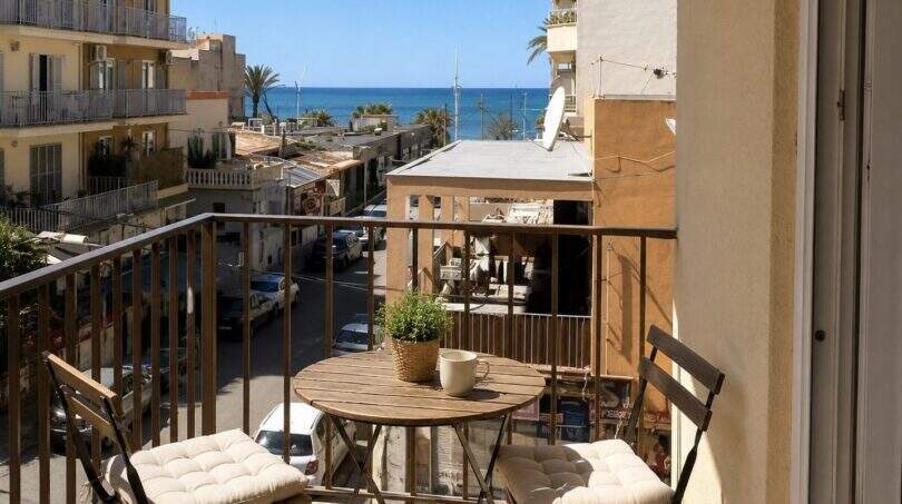 Sonniger Balkon mit Holztisch und Stühlen, Blick über Palmas Dächer und Palmen bis zum Mittelmeer.
