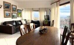 Living-dining area of the penthouse with wooden table, leather sofa, paintings and balcony with panoramic views over Palma