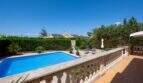Sonniger Poolbereich mit blauem Wasser, Steinterrasse und Balustrade, umgeben von Hecken und Palmen in Llucmajor