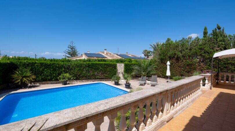 Sonniger Poolbereich mit blauem Wasser, Steinterrasse und Balustrade, umgeben von Hecken und Palmen in Llucmajor