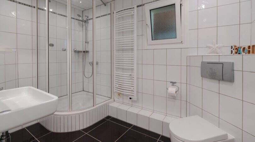 Helles Badezimmer mit Eckdusche, Wandtoilette, Heizkörper und weißen Fliesen im Bungalow Llucmajor
