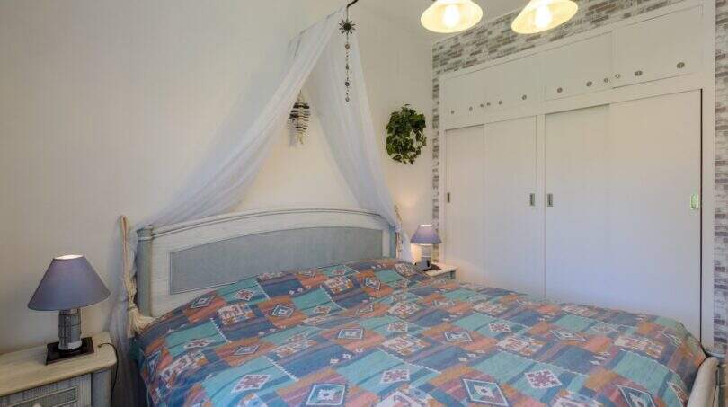 Schlafzimmer mit Doppelbett, Baldachin, bunter Tagesdecke und weißem Einbauschrank im mediterranen Bungalow.