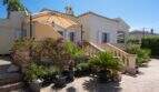 Mediterrane Villa in Llucmajor mit Terrassenpatio, Pergola, Topfpflanzen und steinerner Balustrade unter blauem Himmel.