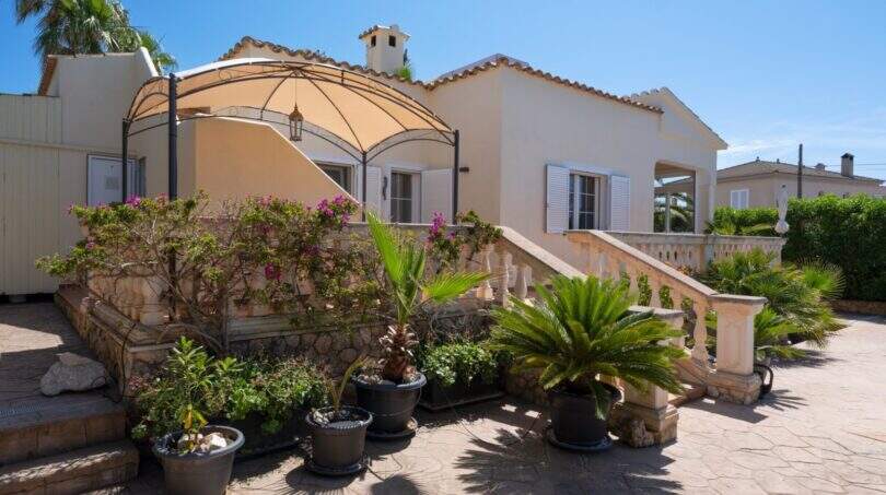 Mediterrane Villa in Llucmajor mit Terrassenpatio, Pergola, Topfpflanzen und steinerner Balustrade unter blauem Himmel.