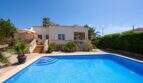 Bungalow mediterráneo en Llucmajor con gran piscina, terraza y palmeras bajo cielo azul.