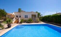 Mediterranean bungalow in Llucmajor with large swimming pool, terrace and palm trees under blue sky.