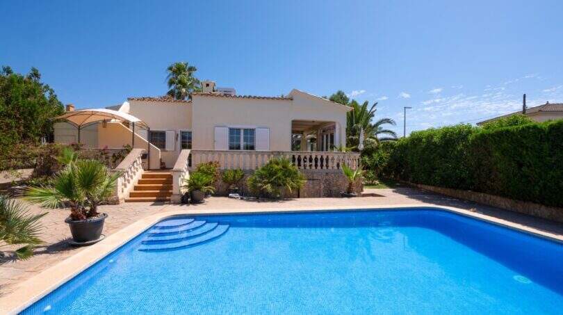 Bungalow mediterráneo en Llucmajor con gran piscina, terraza y palmeras bajo cielo azul.