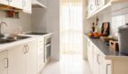 Helle Galley-Küche mit weißen Schränken, Einbauofen und Tür zum Balkon im Penthouse Palma