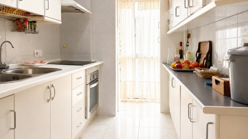 Helle Galley-Küche mit weißen Schränken, Einbauofen und Tür zum Balkon im Penthouse Palma