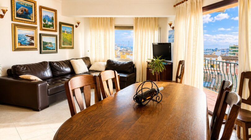 Helles Wohn-Esszimmer mit Holztisch, Ledersofa und Balkon mit Panoramablick über Palma de Mallorca