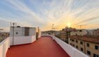 Großzügige Dachterrasse des Penthouse mit rotem Boden, weißer Brüstung und Sonnenuntergang über Palma