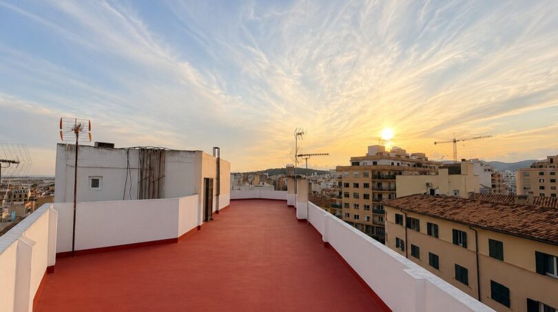 Großzügige Dachterrasse des Penthouse mit rotem Boden, weißer Brüstung und Sonnenuntergang über Palma