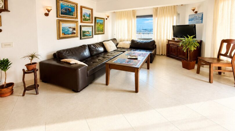 Helles Wohnzimmer des Penthouses mit Ledersofa, Gemälden, Pflanzen und Meerblick durch große Fenster.