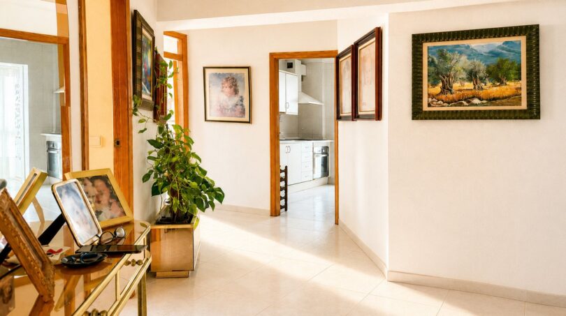 Heller Eingangsbereich des Penthouses in Palma mit Gemälden, Holztüren und Blick in die moderne Küche.