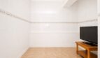 Helles Zimmer mit weißen Wandfliesen, Fliesenboden und LG-Flachbildfernseher auf Holzschrank im Penthouse Palma.