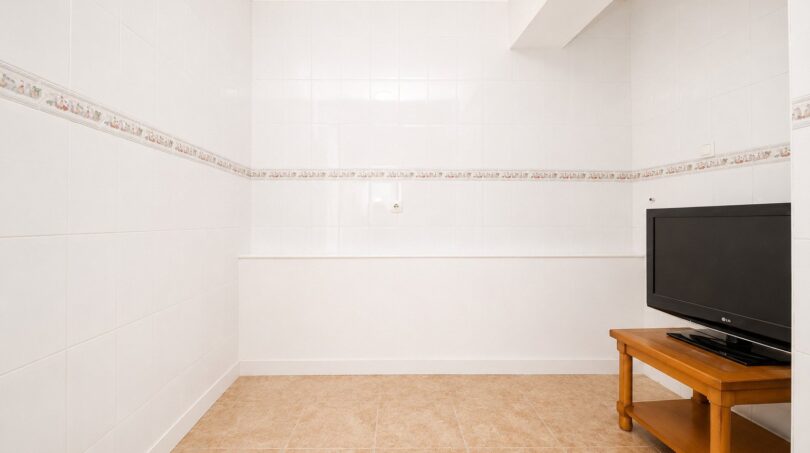 Helles Zimmer mit weißen Wandfliesen, Fliesenboden und LG-Flachbildfernseher auf Holzschrank im Penthouse Palma.