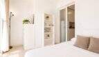 Helles Schlafzimmer im Penthouse Palma de Mallorca mit weißem Bett, Regal und Blick in offene Küche.