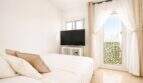 Helles Schlafzimmer im Penthouse Palma de Mallorca mit Doppelbett, TV und Balkonzugang mit Grünpflanzen.