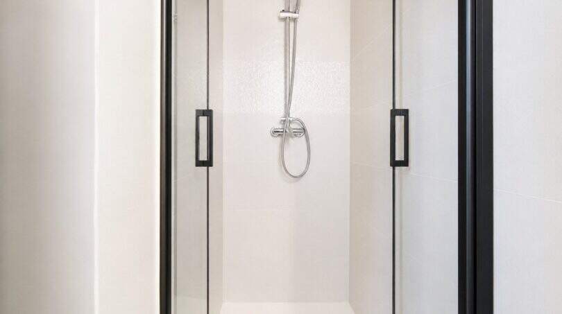 Modernes Duschbad im Penthouse mit weißen Wandfliesen, Glasduschkabine und schwarzen Akzenten.