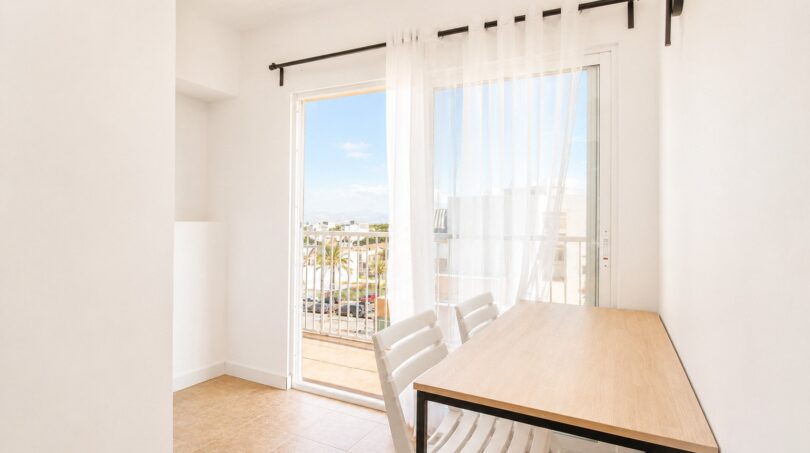 Heller Essbereich mit Holztisch, weißen Stühlen und Balkonzugang mit Meerblick im Penthouse Palma de Mallorca