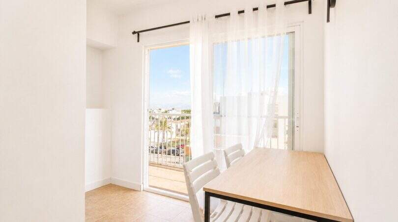 Helles Esszimmer im Penthouse Palma de Mallorca mit Holztisch, weißen Stühlen und Balkon mit Meerblick.