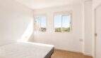 Helles Schlafzimmer im Penthouse Palma de Mallorca mit weißen Wänden, Doppelbett und Stadtblick durch zwei Fenster.