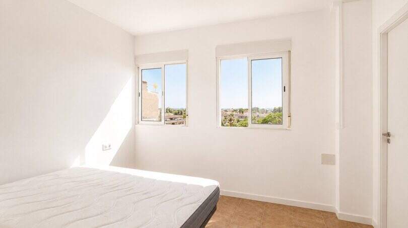 Helles Schlafzimmer im Penthouse Palma de Mallorca mit weißen Wänden, Doppelbett und Stadtblick durch zwei Fenster.