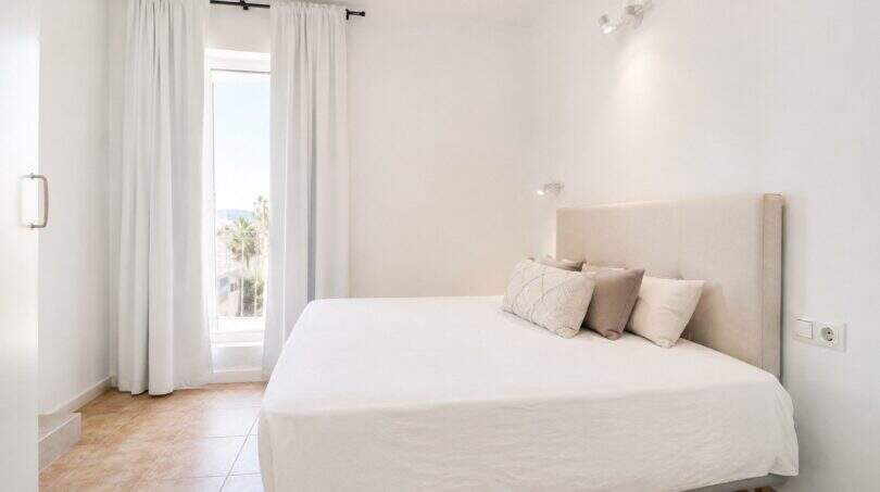 Helles Schlafzimmer im Penthouse Palma de Mallorca mit Doppelbett, weißen Wänden und Fenster mit Palmenblick.