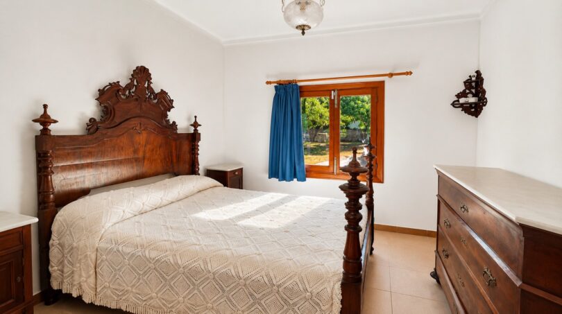 Schlafzimmer der Finca Sencelles mit antikem Holzbett, Kommode und Fenster zum Garten