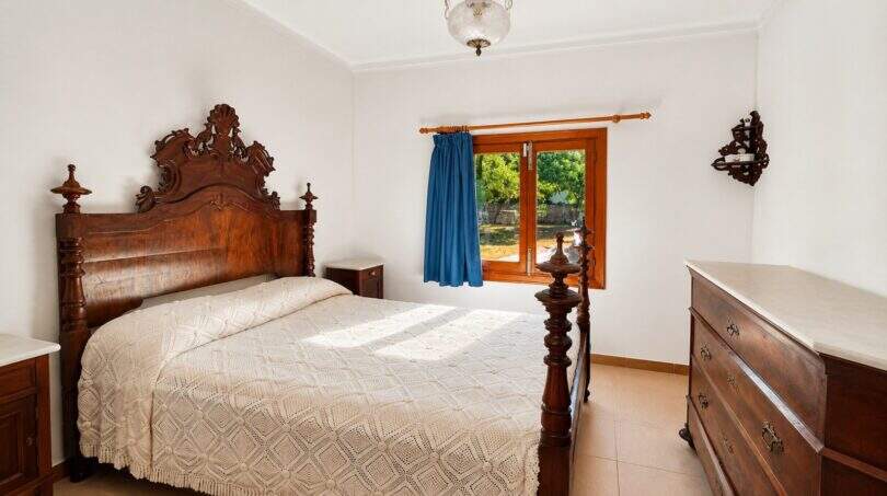 Schlafzimmer der Finca bei Sencelles mit antikem Holzbett, Kommode und Fenster zum Garten.