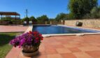 Finca Sencelles: Gepflasterter Poolbereich mit Blumentopf, Steinmauer und Pergola unter blauem Himmel