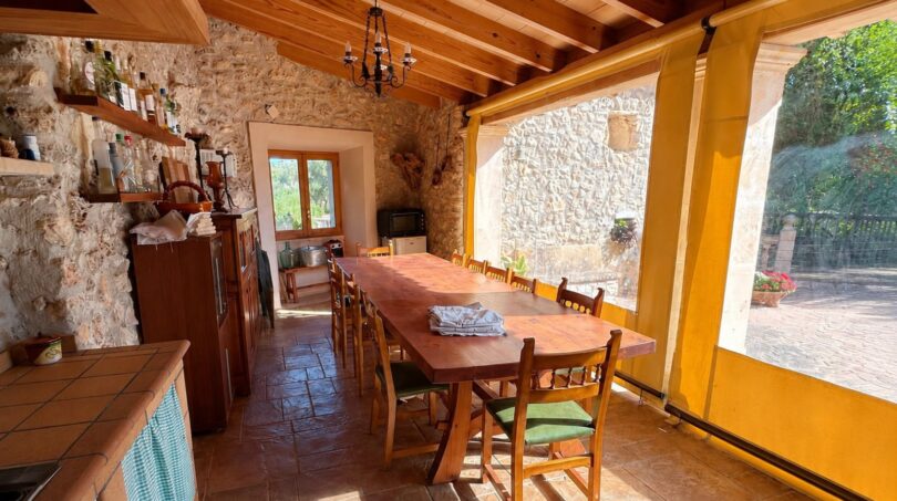 Rustikale Terrasse der Finca Sencelles mit langem Holztisch, Natursteinwänden und gelbem Sonnenschutz