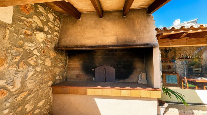 Rustikaler Außenbereich der Finca mit gemauertem Holzofen, Natursteinwand und überdachter Terrasse.